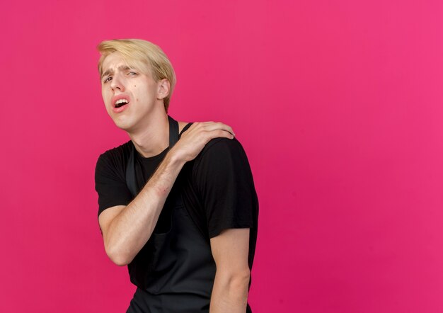 Professionele kapper man in schort aanraken van zijn schouder pijn voelen op zoek onwel