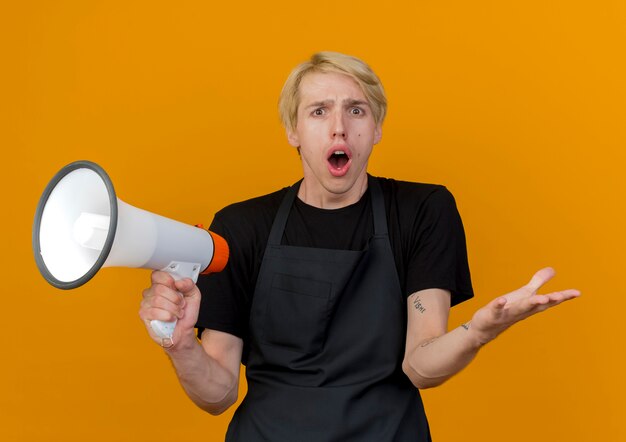 Professionele kapper man in schort met megafoon kijken voorkant wordt verrast en verward staande over oranje muur