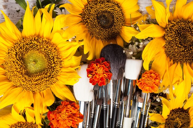 Professionele make-upborstels naast mooie wilde bloemen op houten achtergrond