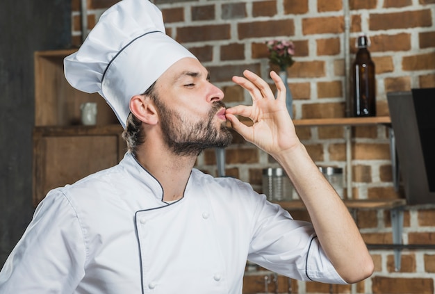 Professionele mannelijke chef-kok die teken voor heerlijk toont