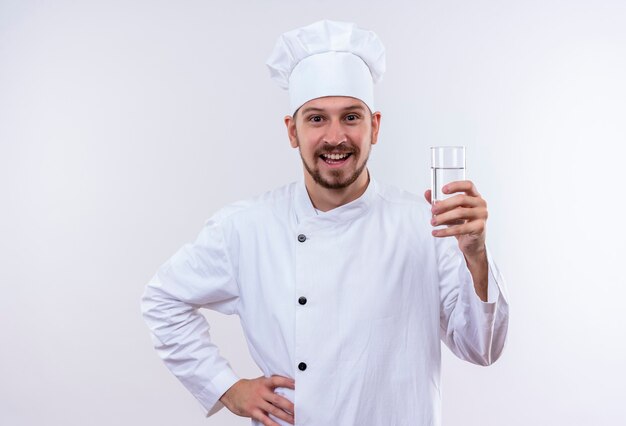 Professionele mannelijke chef-kok in wit uniform en kok hoed met een glas water glimlachend vrolijk staande op witte achtergrond