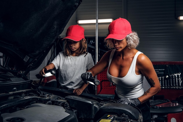 Professionele monteurvrouw en haar kleine helper vormen een geweldig team en werken aan de motor van de auto.