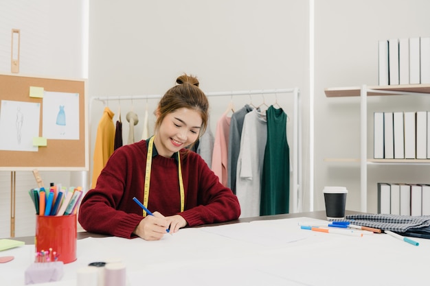 Professionele mooie Aziatische vrouwelijke modeontwerper werken met stoffen schetsen