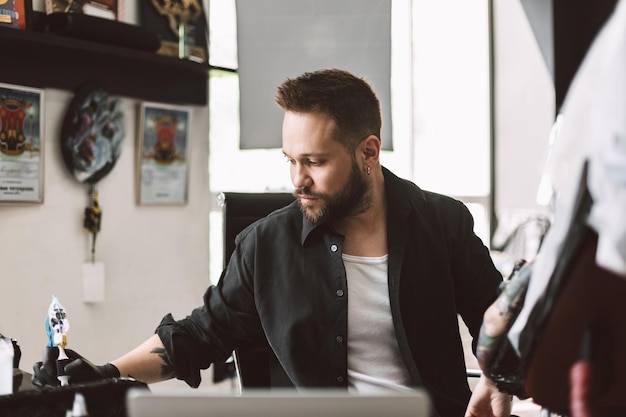 Professionele tatoeëerder die tatoeage doet door tattoo-machine tijd door te brengen in moderne tattoo-studio