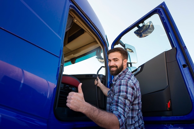 Gratis foto professionele vrachtwagenchauffeur zijn lange voertuig van de vrachtwagen invoeren en duimen omhoog te houden