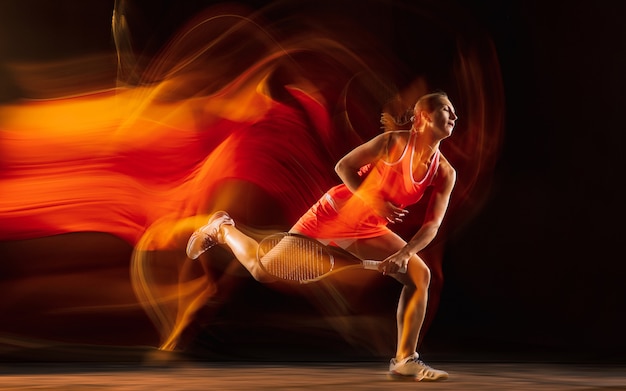 Professionele vrouwelijke tennisspeelster training geïsoleerd op zwarte studio achtergrond in gemengd licht. Vrouw in sportpak oefenen.