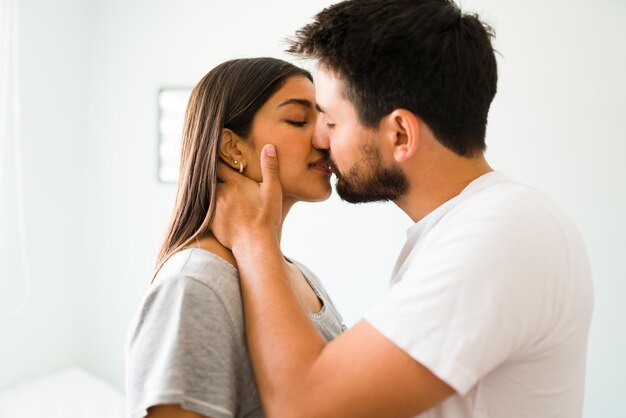 Profiel van een prachtige vrouw en een latijnse man die een comfortabele pyjama draagt en een sensuele kus deelt voordat ze naar bed gaan