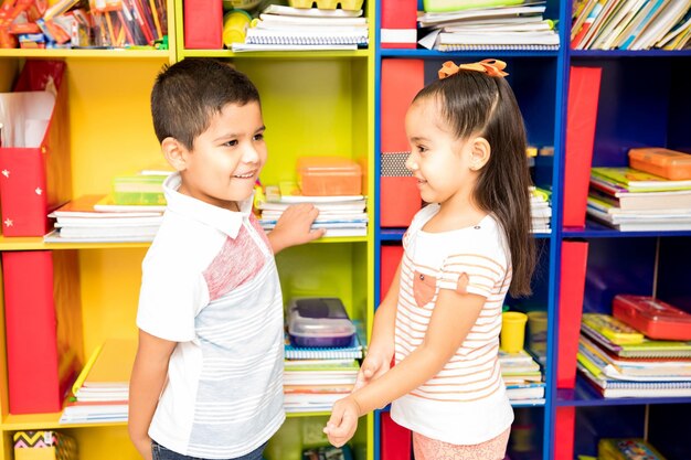 Profielweergave van een verlegen jongetje en een meisje die met elkaar flirten terwijl ze voor een klaslokaal staan
