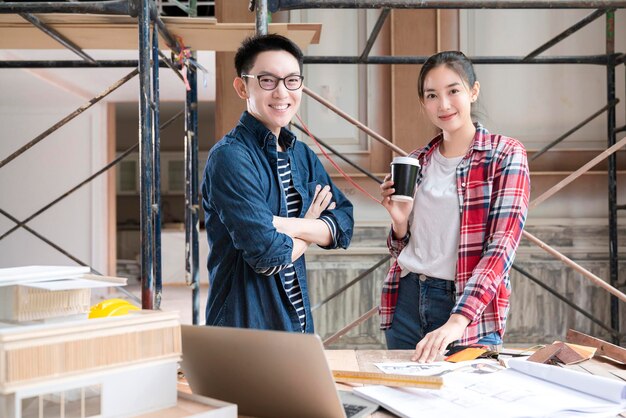 Raadplegingsvergadering van twee slimme mannelijke vrouwelijke aziatische interieurontwerpers of architecten met een blauwdrukhuismodel en materiaalmonster met gelukkig thuis renoveren verbeteringsplaatsbouwachtergrond