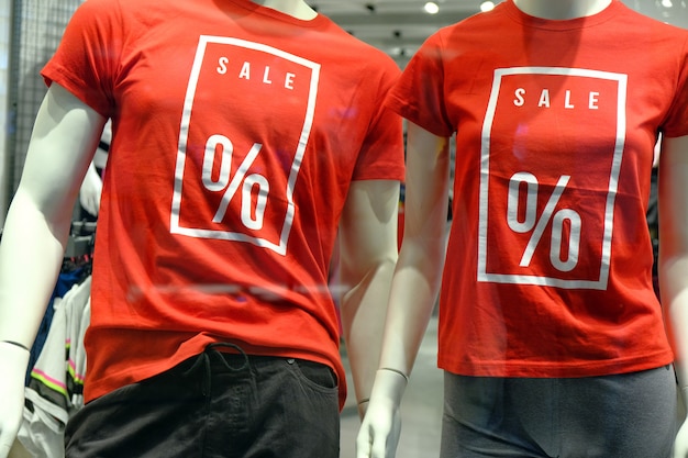 Raam van boetiek met twee mannequins in t-shirts met borden met reclameverkoop voor sportkleding.