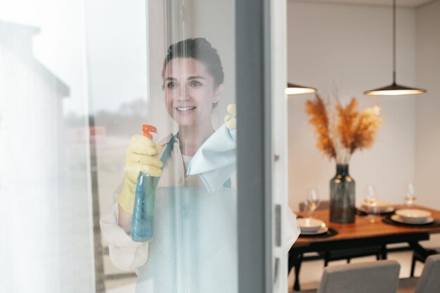 Ramen schoonmaken. Een vrouw in schort die de ramen schoonmaakt en er betrokken uitziet