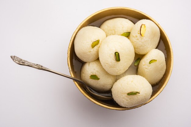 Rasgulla of rosogulla - een indiaas snoepje gemaakt van khoya, zacht en sponsachtig, in aarden kom over gele servet en bruine achtergrond