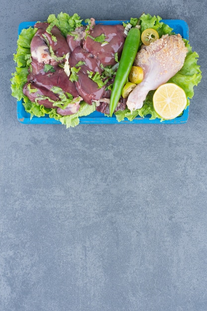 Rauw vlees en kippenbeen op blauw bord.