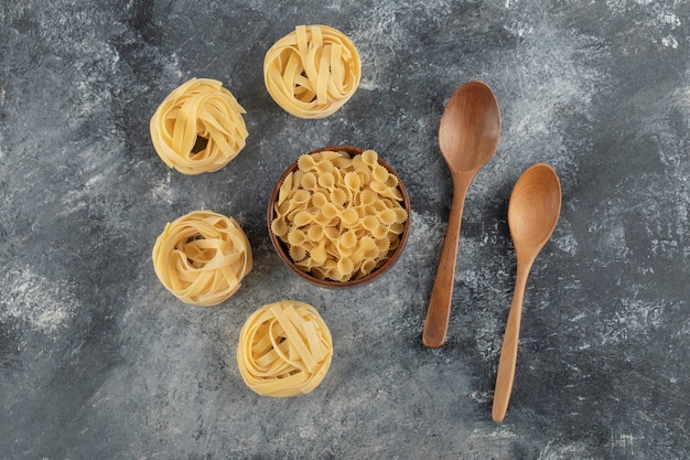 Rauwe droge nestnoedels met farfalle tonde pasta op een marmeren tafel.