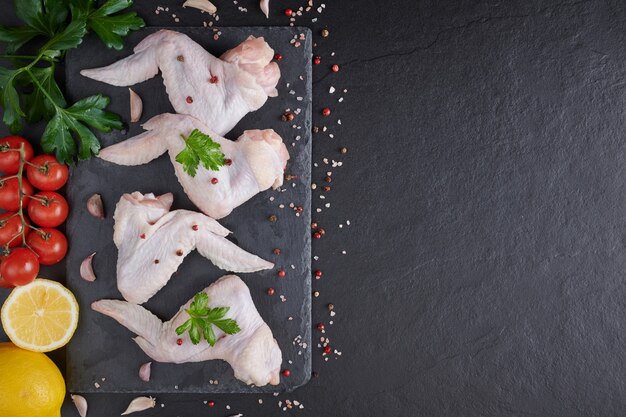 Rauwe kippenvleugels met ingrediënten om te koken. Rauw vlees. Kippenvleugels liggen op een houten bord met groenten en kruiden op een zwarte achtergrond.