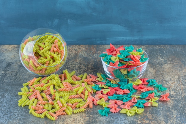 Rauwe kleurrijke farfalle en fusilli pasta, op het marmeren oppervlak.