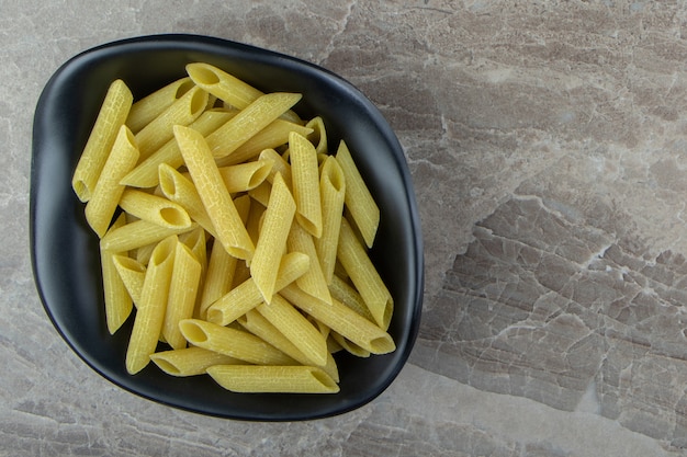 Rauwe penne pasta in zwarte kom.