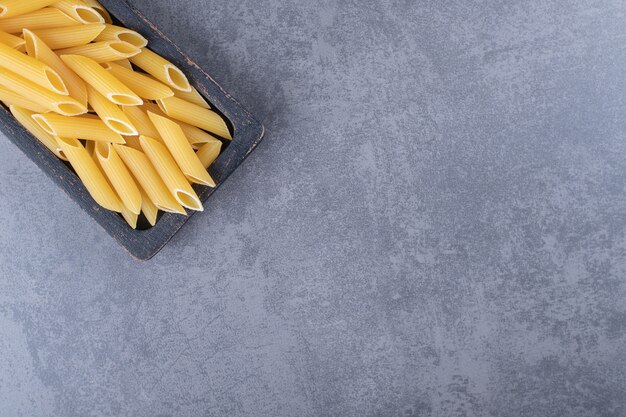 Rauwe penne pasta op zwarte plaat.