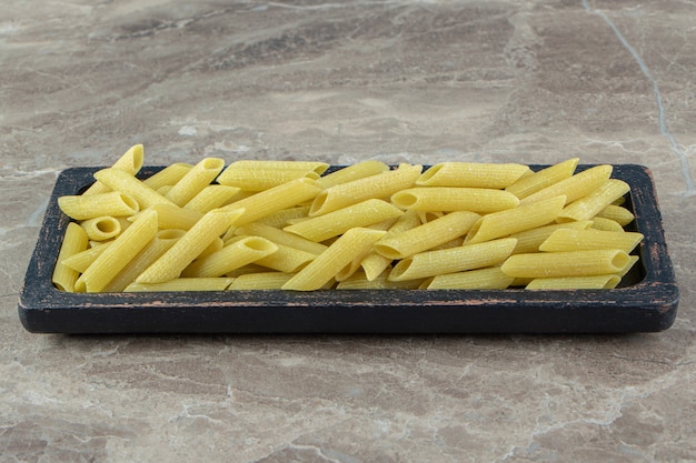 Gratis foto rauwe penne pasta op zwarte plaat.