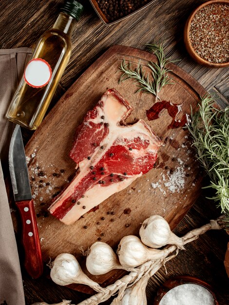 Raw t-bone steak met zwarte peper en rozemarijn aan boord geserveerd