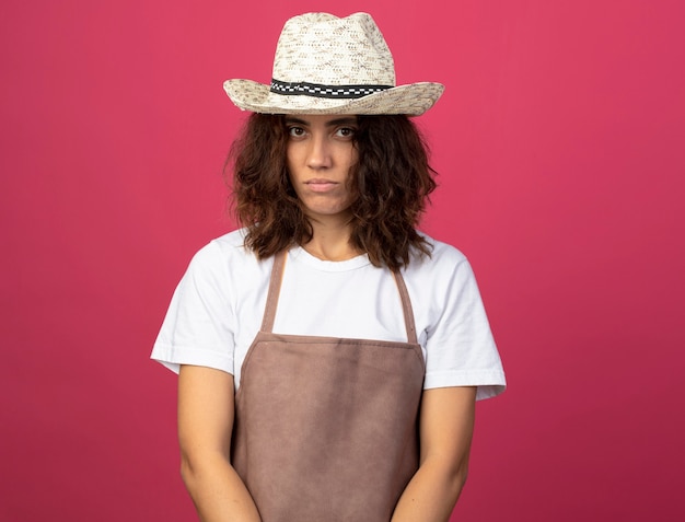 rechtdoor kijken jonge vrouwelijke tuinman in uniform dragen tuinieren hoed geïsoleerd op roze