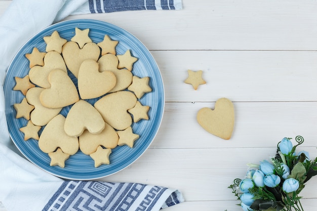 Gratis foto reeks bloemen en koekjes in een plaat op houten en keukenhanddoekachtergrond. plat leggen.