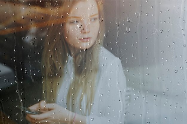 Regenachtige vensterachtergrond, vrouw die een telefoon gebruikt