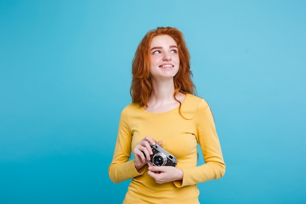 Reis concept - Close-up Portret jonge mooie aantrekkelijke roodharige meisje wtih trendy hoed, zonnebril en vintage camera lachend naar camera. Blauwe Pastelachtergrond. Kopieer de ruimte.