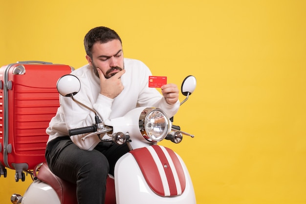 Reisconcept met een jonge denkende reizende man die op een motorfiets zit met een koffer erop met een bankkaart op geel