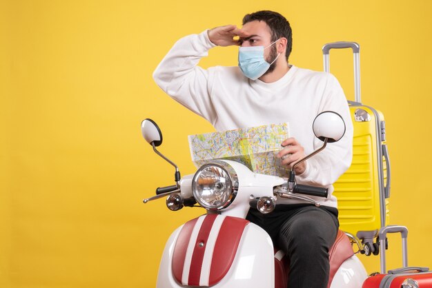 Reisconcept met jonge kerel met medisch masker zittend op motorfiets met gele koffer erop