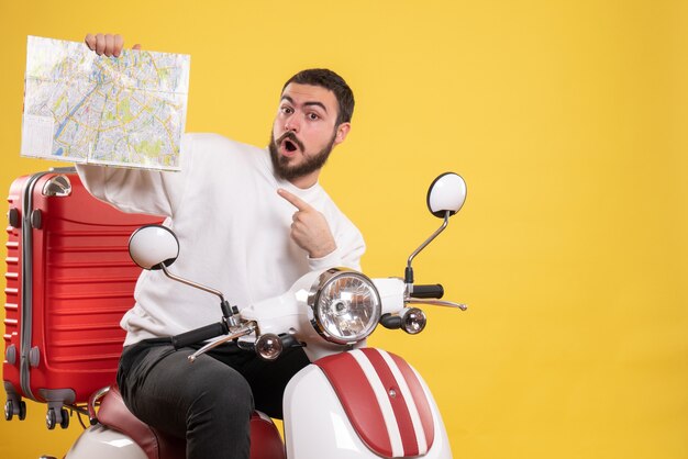 Reisconcept met verraste man zittend op motorfiets met koffer erop wijzende kaart op geel?