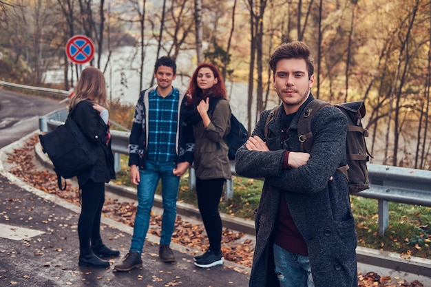 Reizen, liften, avontuur concept. Groep jonge wandelaars die aan de zijlijn van de weg staan in een prachtig herfstbos