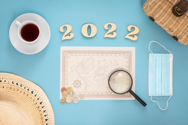 Reizen plat lag compositie met wereldkaart en nummers 2022 op blauwe achtergrond.