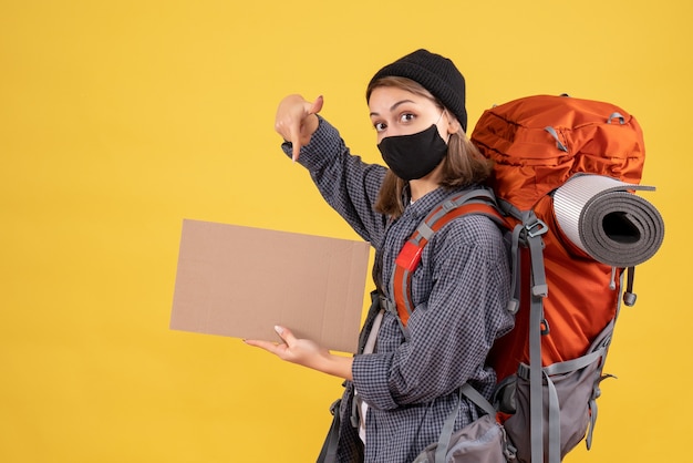 Reizigersmeisje met zwart masker en rugzak wijzend op karton