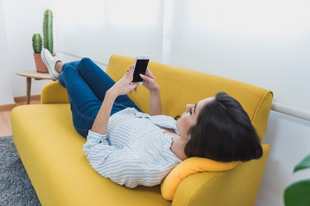 Relaxed jonge zakenvrouw liggend op de bank en het gebruik van haar mobiele telefoon