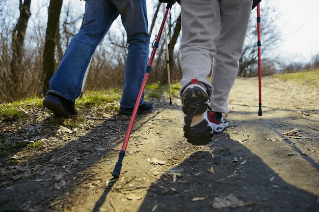 Rennen voor gezondheid. Leeftijd familie paar man en vrouw in toeristische outfit wandelen op groen gazon in de buurt van bomen in zonnige dag. Concept van toerisme, gezonde levensstijl, ontspanning en saamhorigheid.