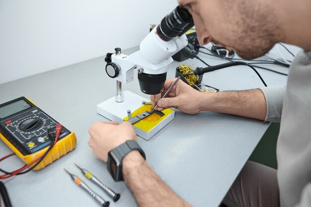 Reparateur onderzoekt het moederbord van de mobiele telefoon onder de Microscoop in laboratorium