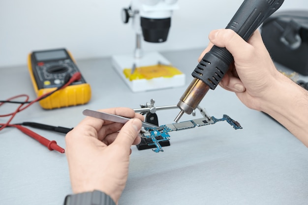 Reparateur soldeert componenten in moederbord tijdens het repareren van beschadigde smartphone, met behulp van een pincet en een strijkijzer