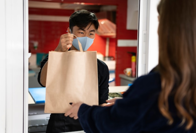 Gratis foto restaurantmedewerker die de bestelling overhandigt aan een klant