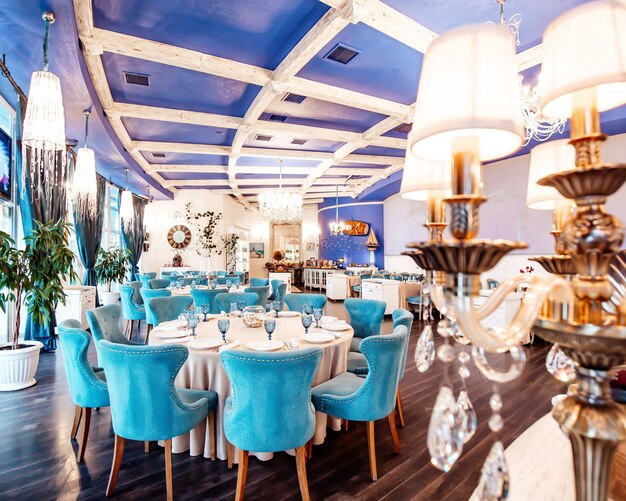 Restaurantzaal met turquoise stoelen, marinekleurig plafond, klassieke kroonluchters en witte muren