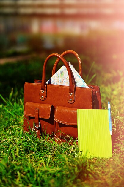 Retro bruine zak en het notitieboekje van het mensenleer in helder kleurrijk de zomergras in het park
