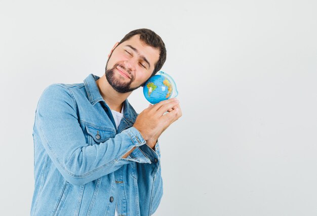 Retro-stijl man in jas, t-shirt leunend op mini globe en kalm, vooraanzicht op zoek. ruimte voor tekst