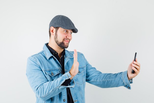 Retro-stijl man in jasje, pet, shirt met afscheidsgebaar terwijl hij een videogesprek voert en er respectvol uitziet, vooraanzicht.