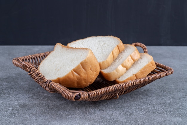 Rieten mand met gesneden wit brood op stenen tafel.