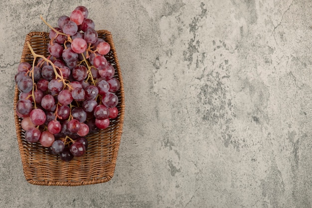 Gratis foto rieten mand met heerlijke rode druiven op marmeren tafel.