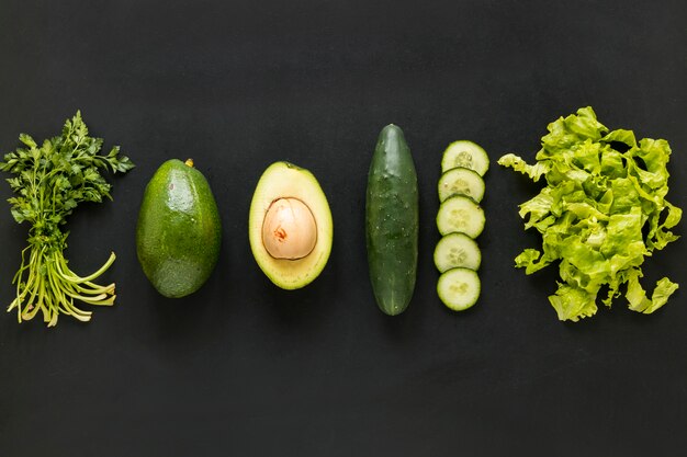 Rij koriander; avocado; komkommer en sla gerangschikt op zwarte achtergrond