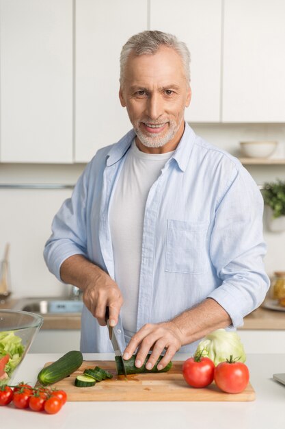 Rijpe aantrekkelijke mens die zich bij keuken het koken bevindt