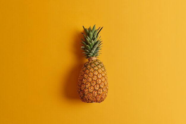 Rijpe ananas geïsoleerd op gele achtergrond. Exotisch fruit met weinig calorieën, boordevol voedingsstoffen en antioxidanten, kan op verschillende manieren worden geconsumeerd of aan uw dieet worden toegevoegd. Ingrediënt voor het maken van sap