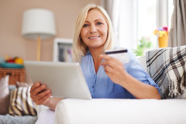 Rijpe blonde vrouw met digitale tablet en creditcard