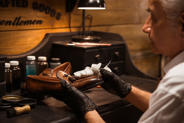 Rijpe schoenmaker die in workshop schoenen maakt